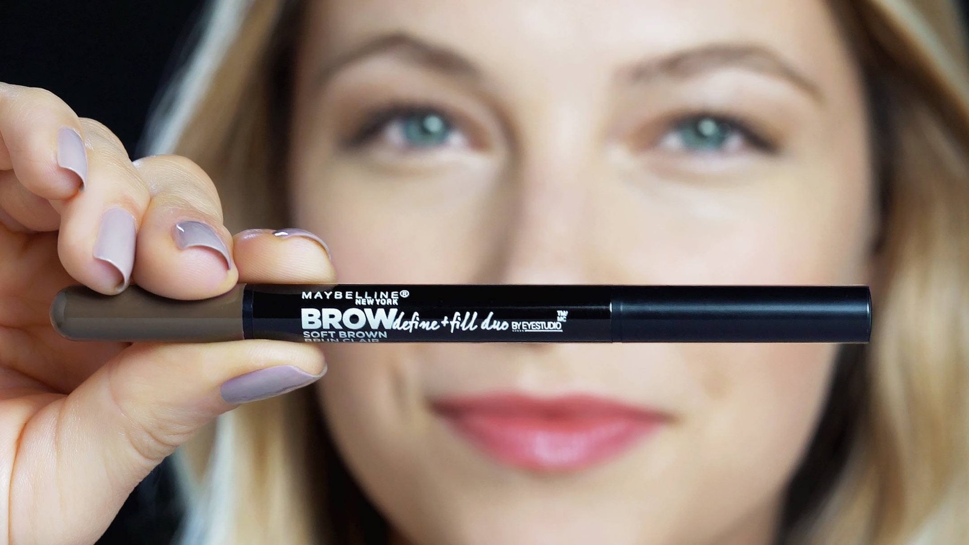 Fokus på en Maybelline Brow Define + Fill Duo-produkt, som en blond kvinna håller i 